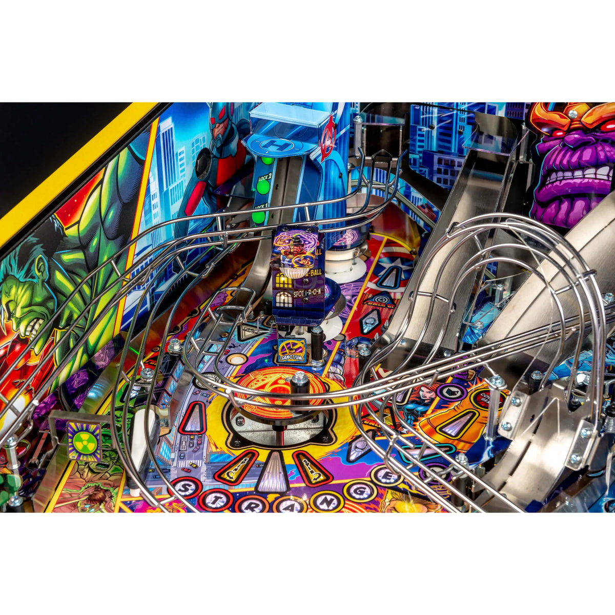 Close-up of a colorful Avengers pinball machine playfield with curved metallic rails, a central target area, and illustrated comic-style graphics including a purple muscular character on the right.